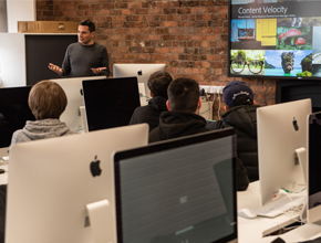 Students working on Macs in a classroom with bare brick walls