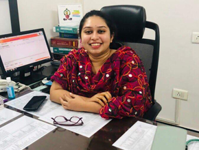 Alumna smiles at camera while sitting at her desk with computer screen on