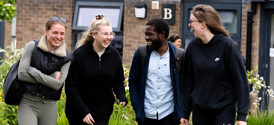 Four students laughing and joking as they walk around campus