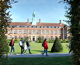 Photo of the HCA building in between two hedges with students walking past